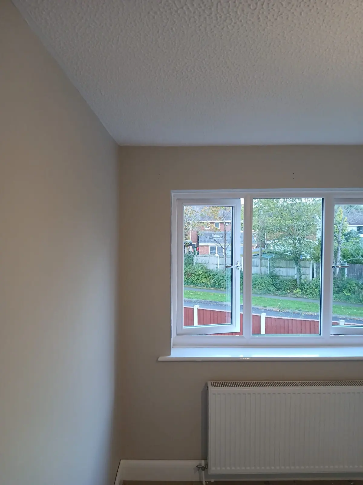 Neutral painted wall and ceiling corner with a white window and radiator looking onto a garden
