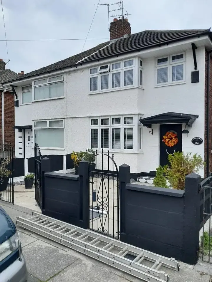 White terraced house with a black front wall, black gate and a ladder resting on the pavement