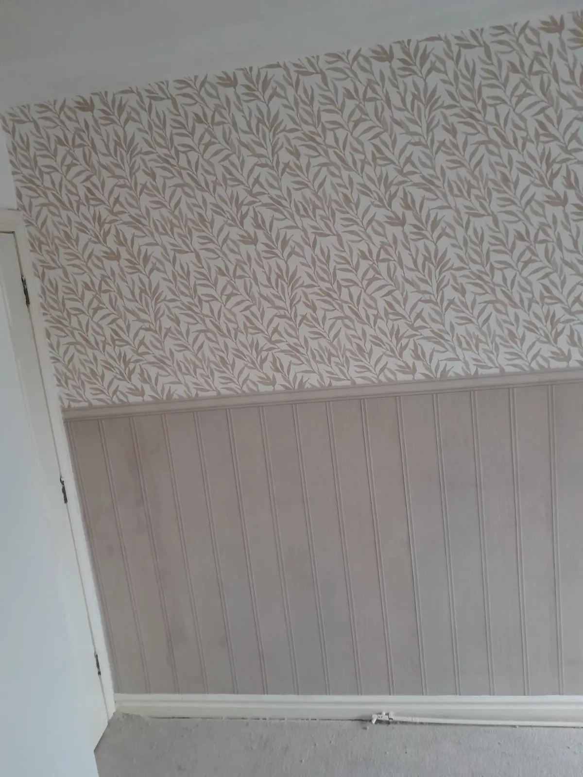 Close view of leaf-patterned wallpaper above pale vertical panelling