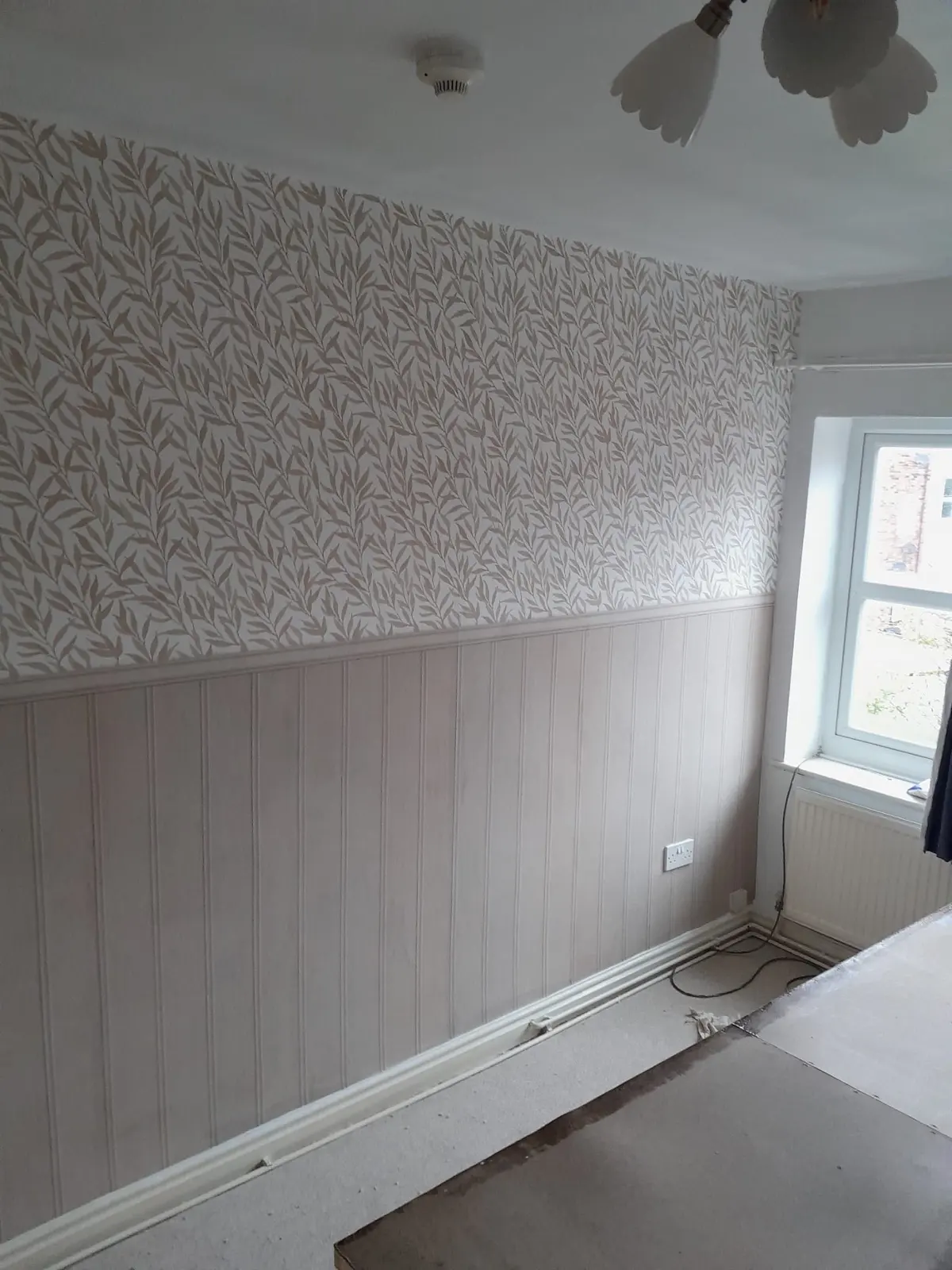 Room with leaf-patterned wallpaper above pale panelling, a window and a radiator